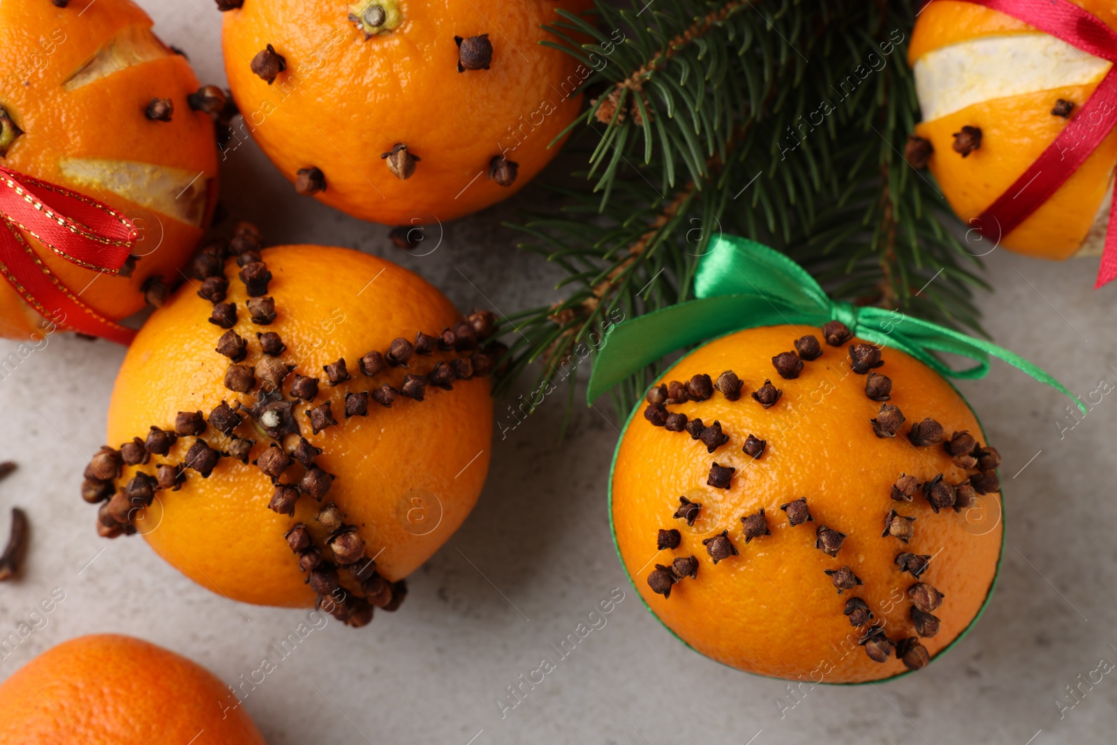 Photo of Pomander balls made of tangerines with cloves and fir branches on grey table, flat lay