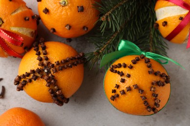 Pomander balls made of tangerines with cloves and fir branches on grey table, flat lay