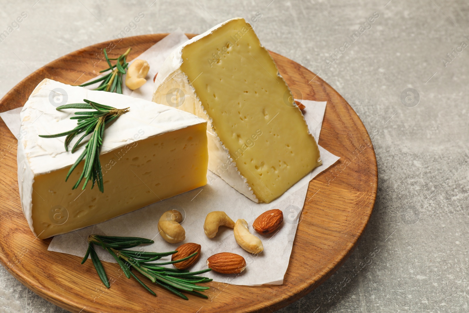 Photo of Plate with pieces of tasty camembert cheese, nuts and rosemary on grey textured table, closeup