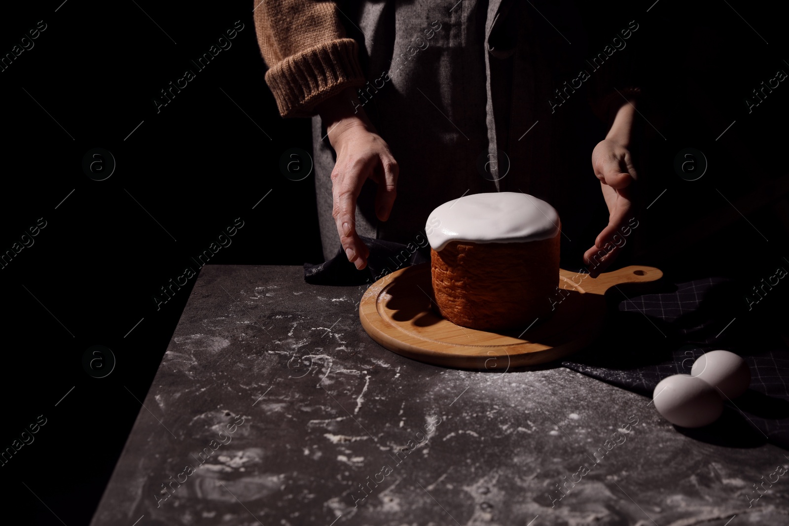 Photo of Young woman making traditional Easter cake at table against black background, closeup. Space for text