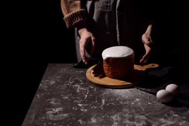 Young woman making traditional Easter cake at table against black background, closeup. Space for text