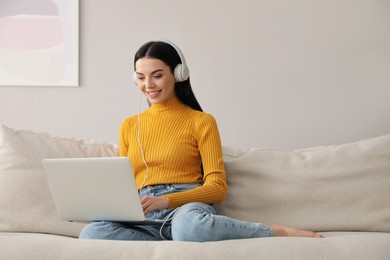 Woman with laptop and headphones sitting on sofa at home