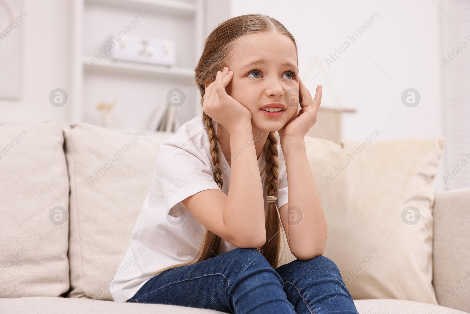 Photo of Little girl suffering from headache on sofa indoors