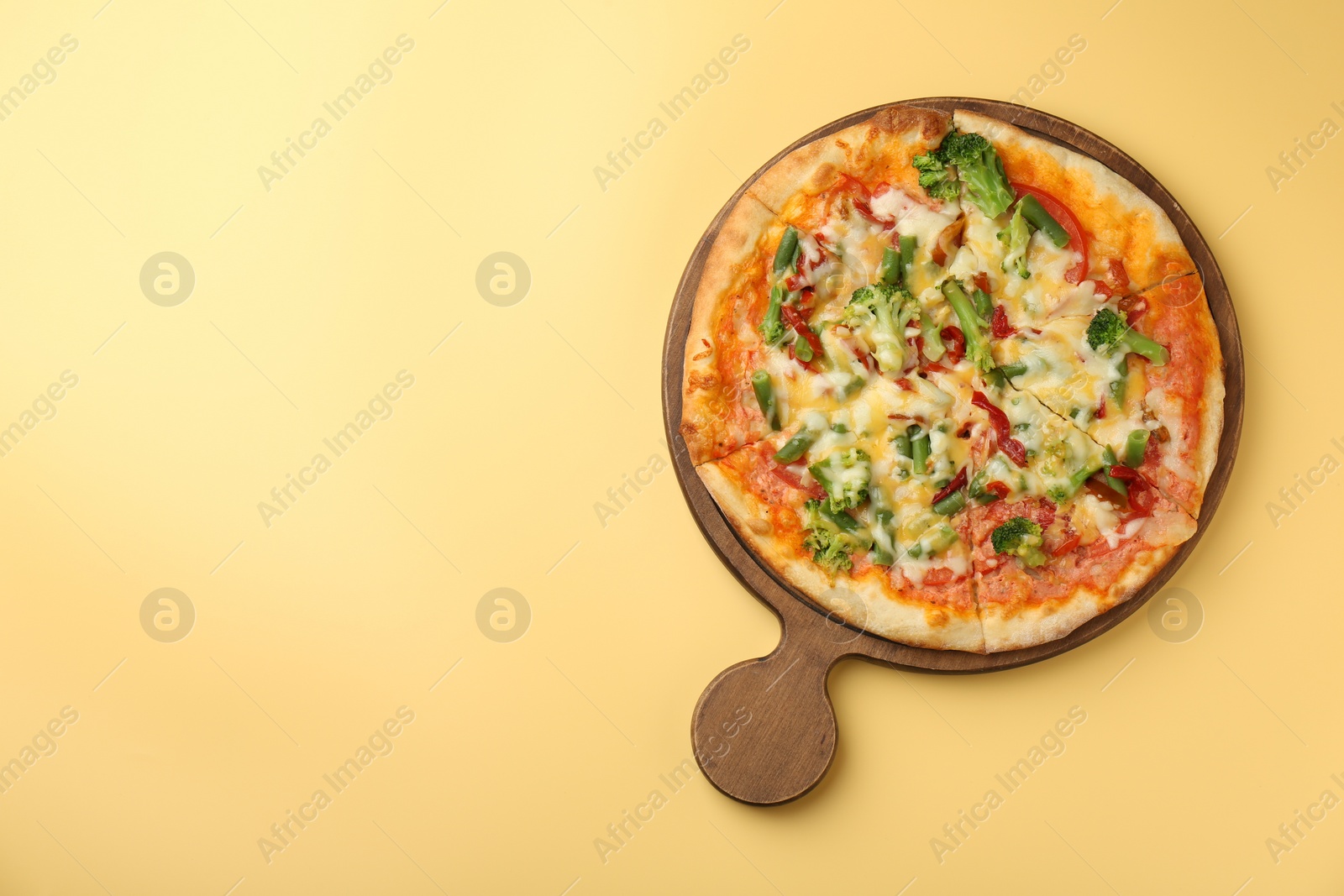 Photo of Board with delicious vegetarian pizza on yellow table, top view. Space for text