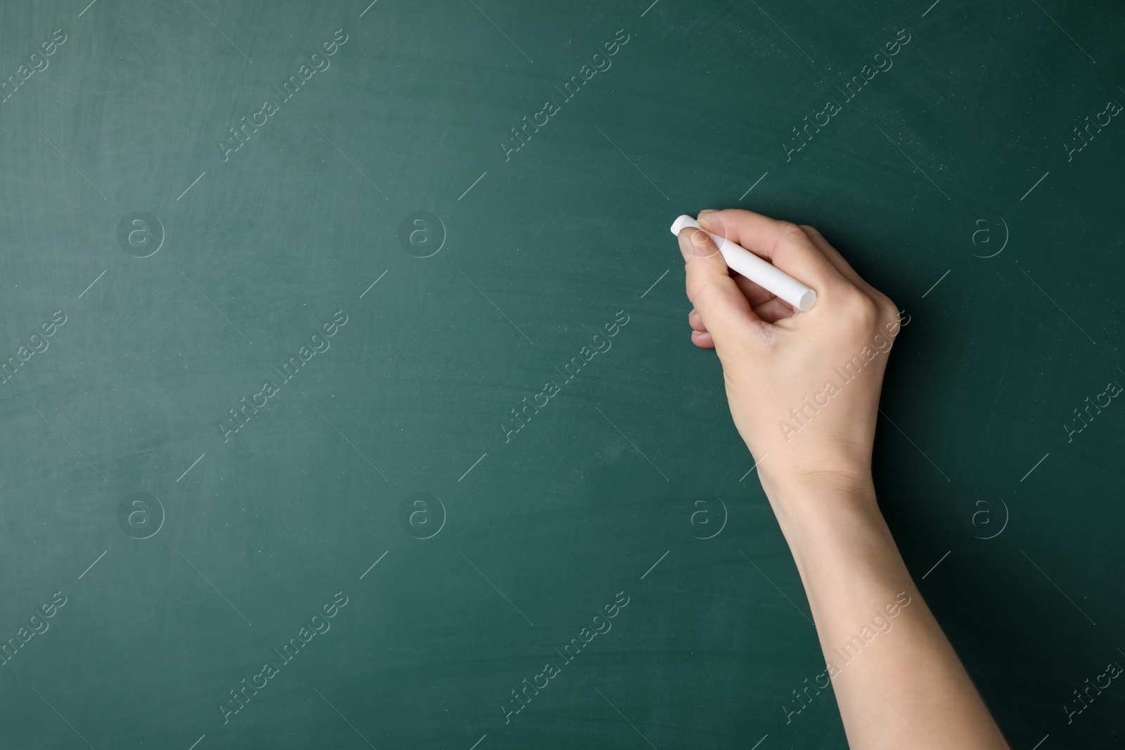 Photo of Woman with white chalk near green blackboard, closeup. Space for text