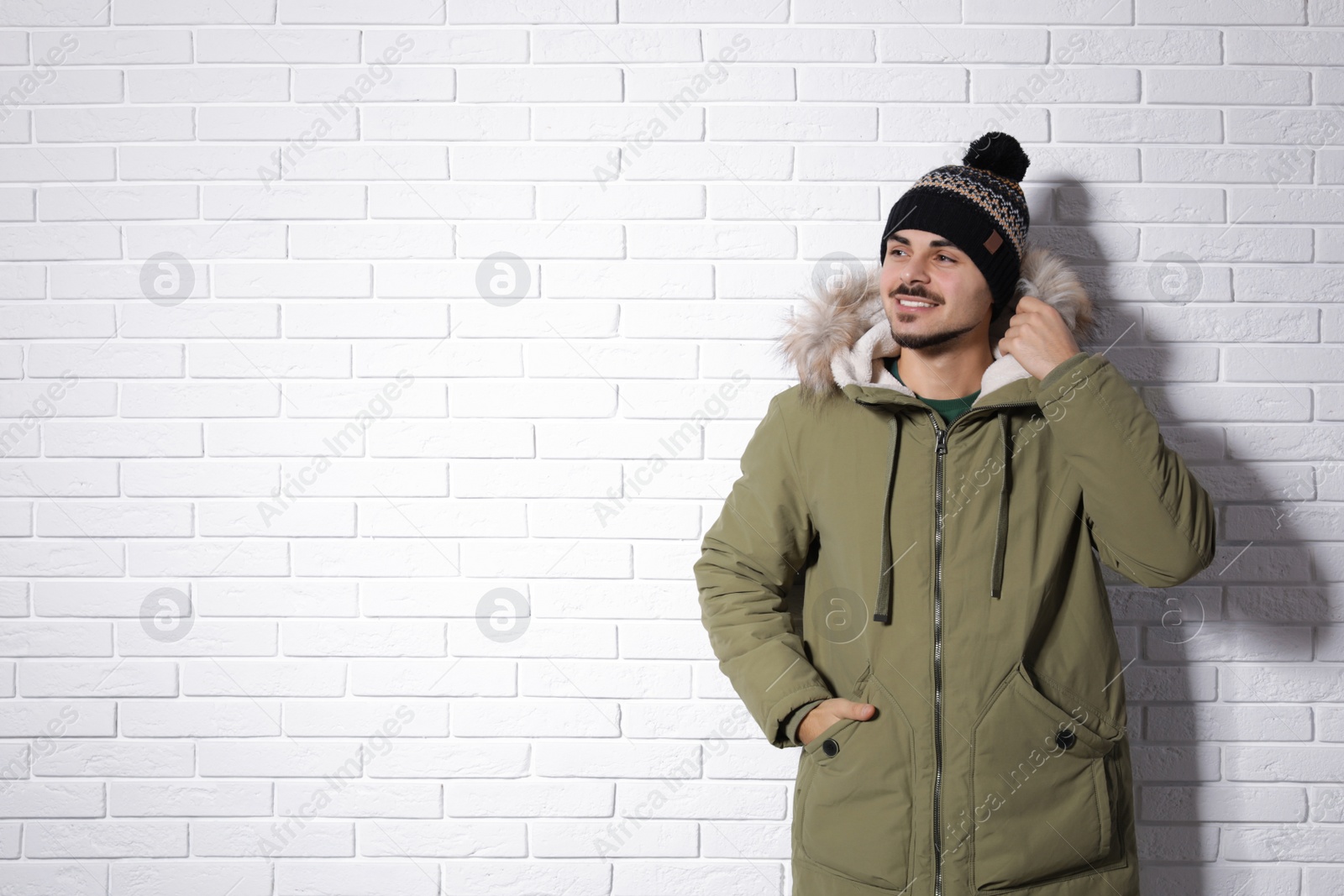 Photo of Young man wearing warm clothes against brick wall, space for text. Ready for winter vacation