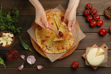 Photo of Top view of woman spreading sauce on delicious khachapuri piece at wooden table