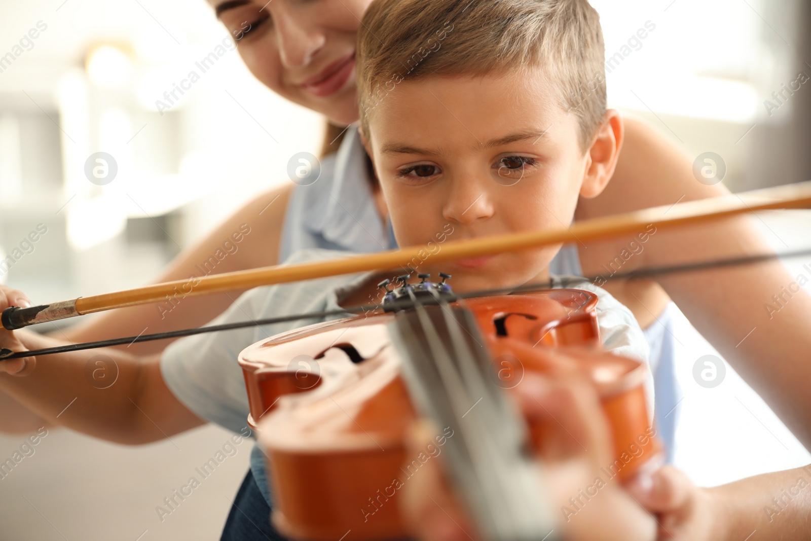 Photo of Young woman teaching little boy to play violin indoors, closeup