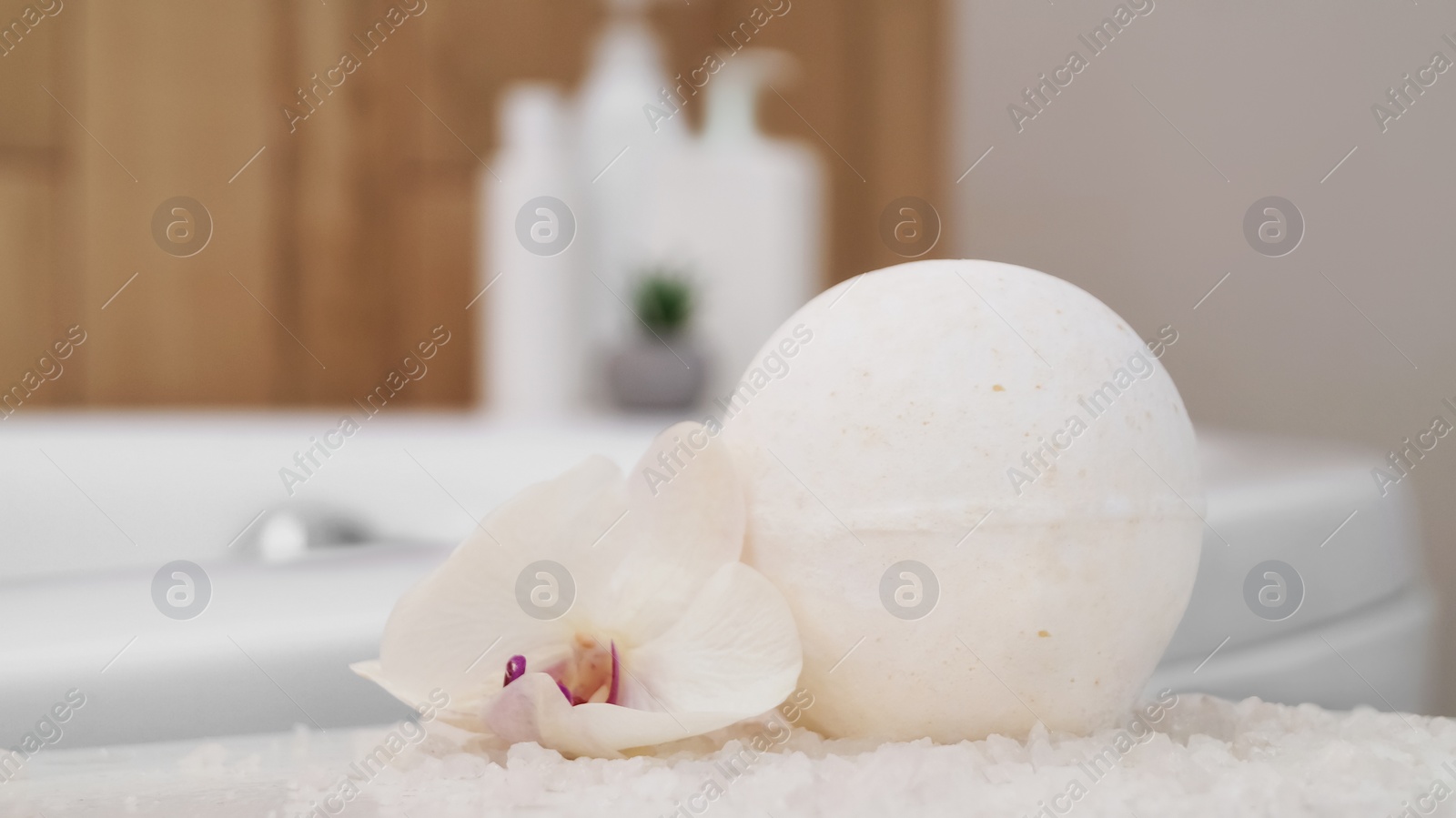 Photo of Bath bomb with orchid and sea salt on table in bathroom, closeup