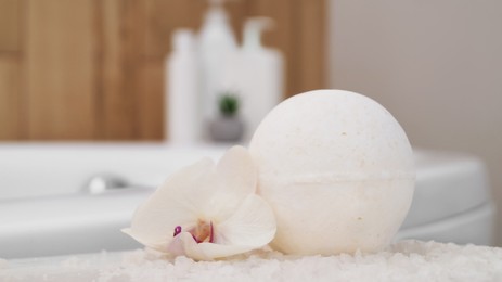 Photo of Bath bomb with orchid and sea salt on table in bathroom, closeup
