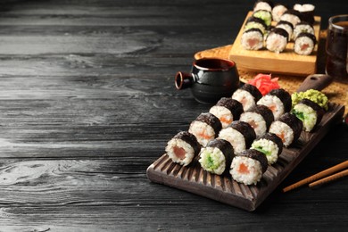Tasty sushi rolls served on black wooden table. Space for text