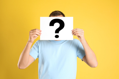Photo of Man holding paper with question mark on yellow background