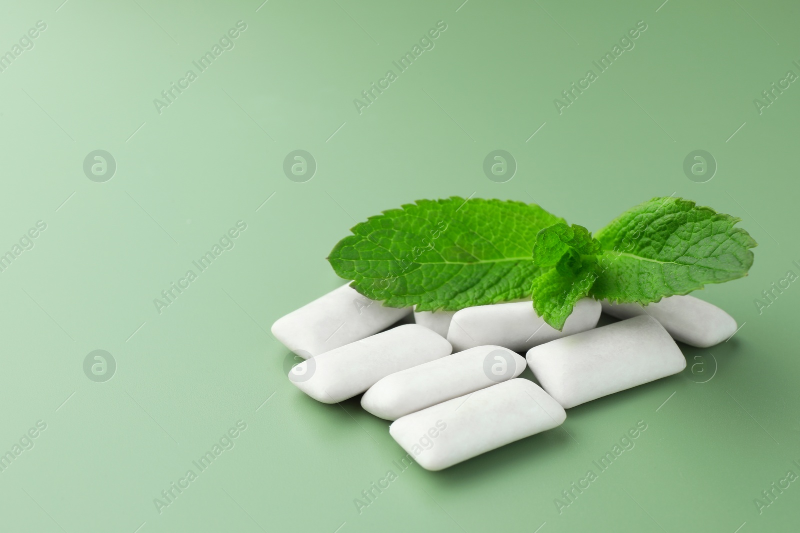 Photo of Tasty white chewing gums and mint leaves on light green background, closeup. Space for text