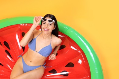 Photo of Happy young woman with beautiful suntan and sunglasses on inflatable mattress against orange background, top view