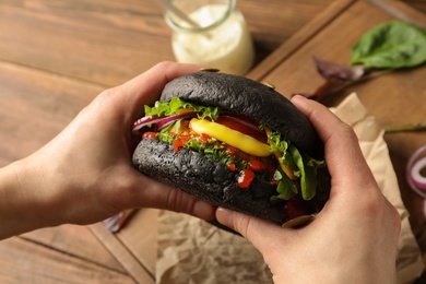 Woman holding tasty black vegetarian burger over table, closeup