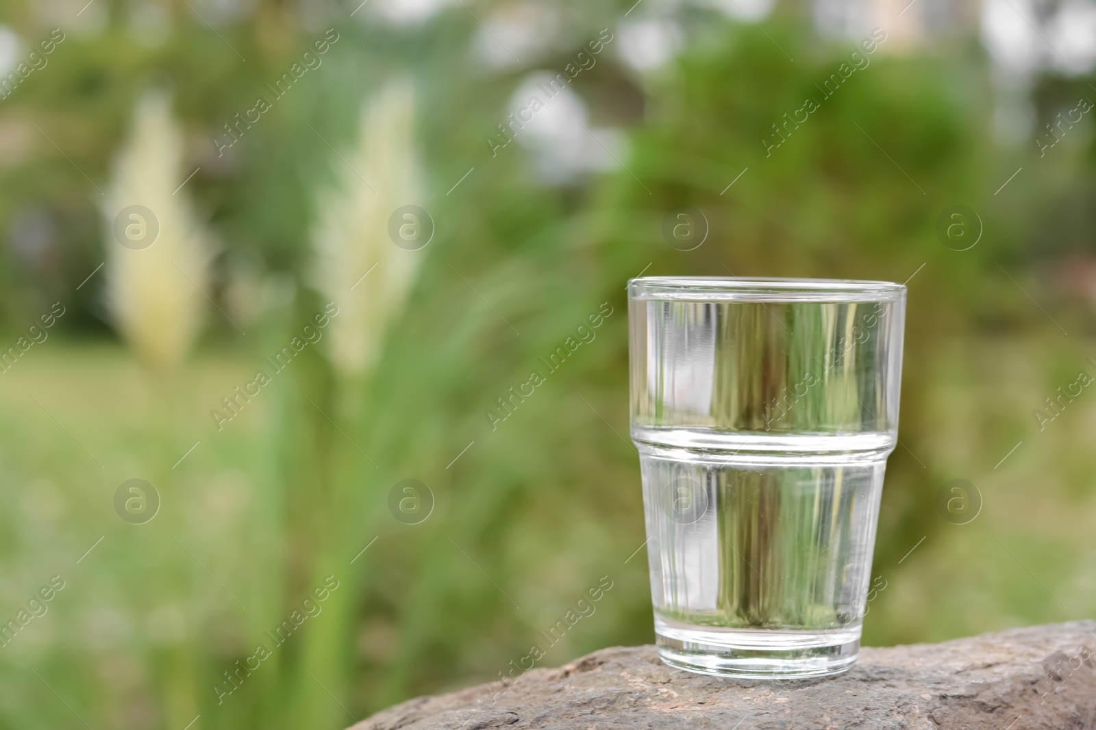 Photo of Full glass of water on stone outdoors, space for text