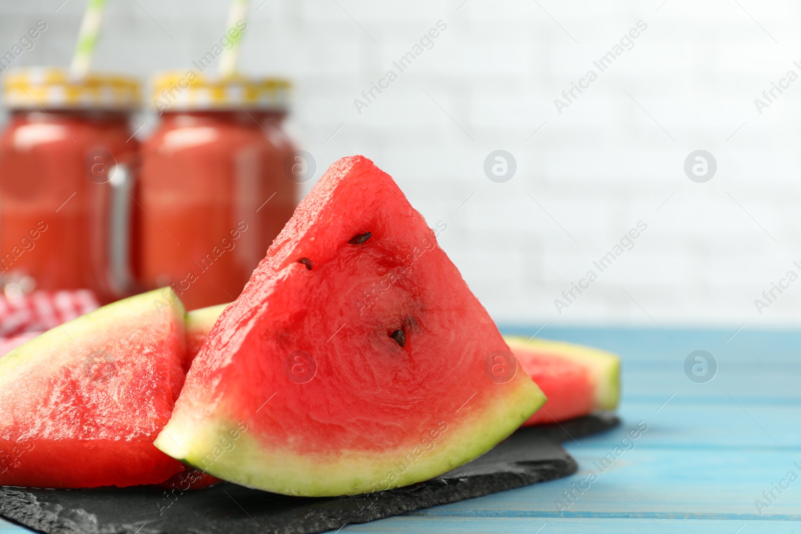 Photo of Slate board with slices of juicy watermelon on light blue wooden table, space for text