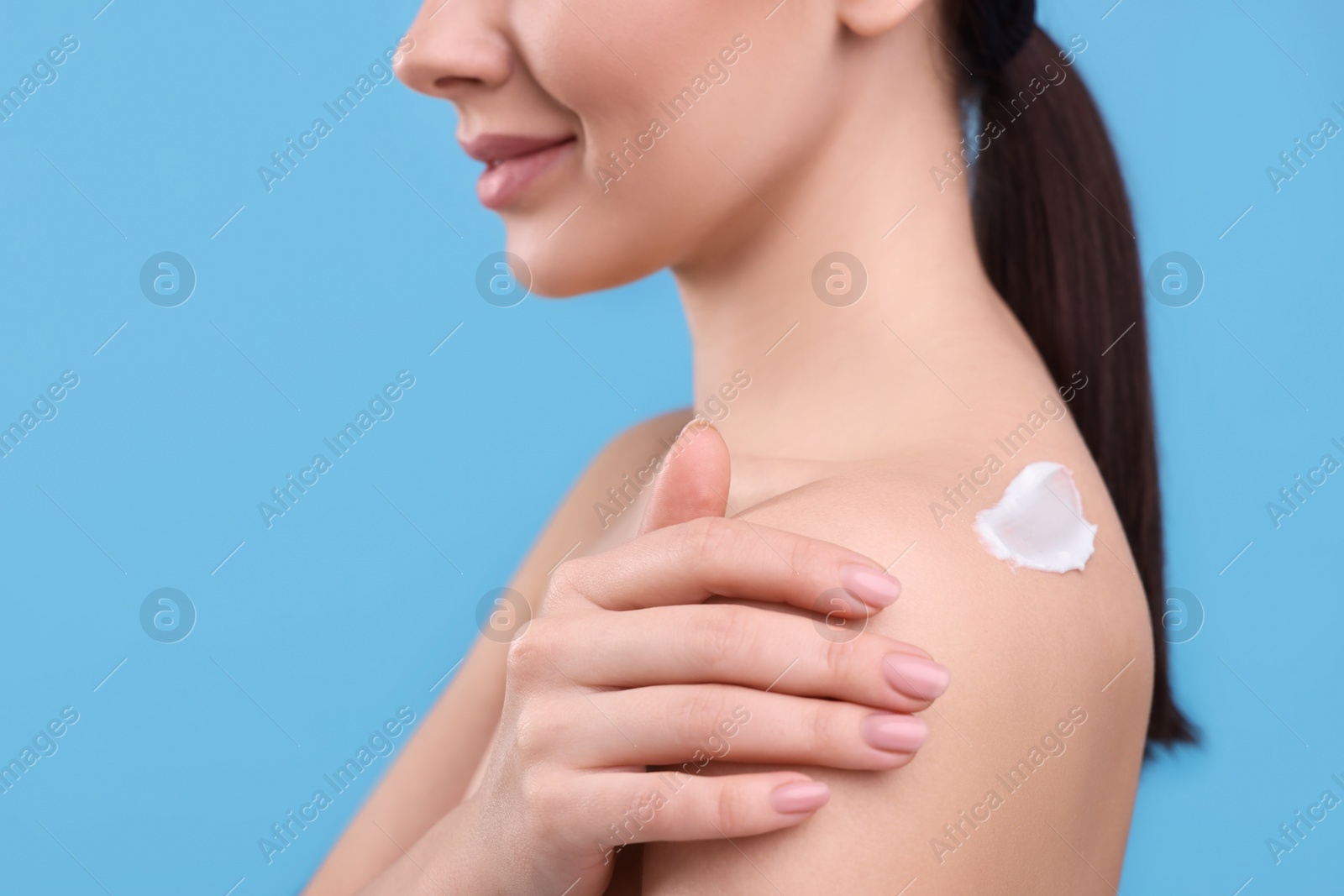 Photo of Woman with smear of body cream on her shoulder against light blue background, closeup