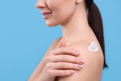 Woman with smear of body cream on her shoulder against light blue background, closeup