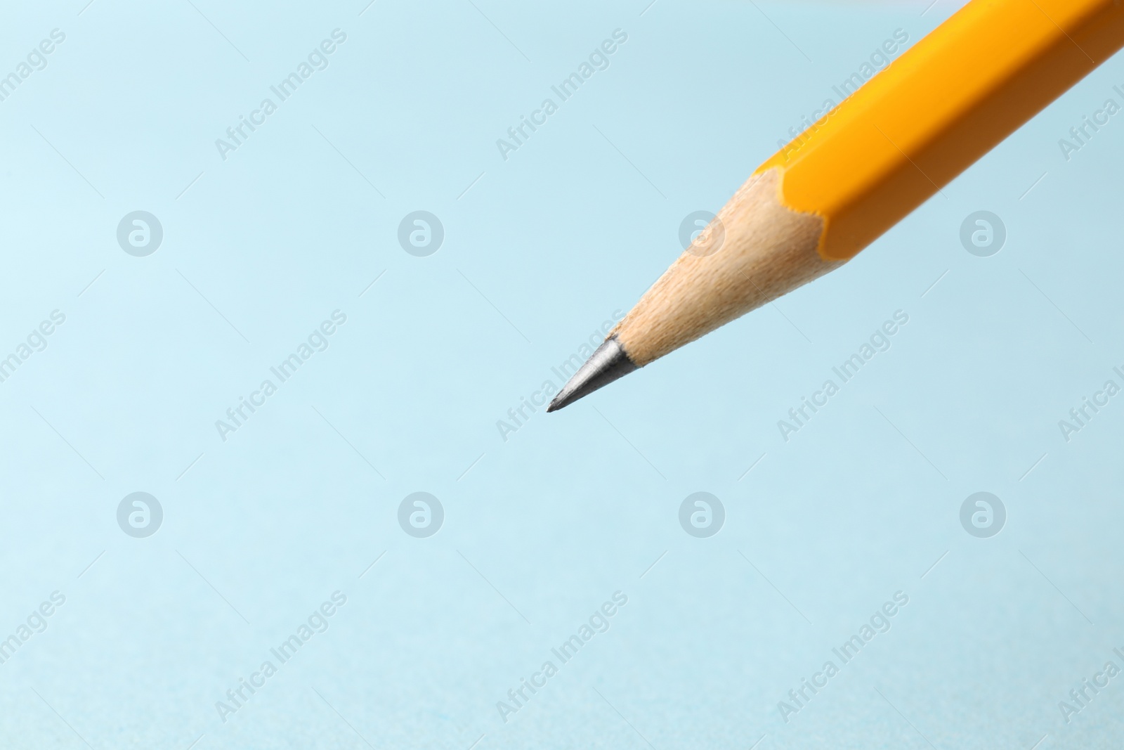 Photo of One sharp graphite pencil on light blue background, closeup. Space for text