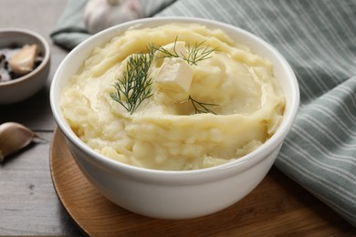 Bowl of delicious mashed potato with dill and butter on wooden table, closeup