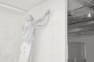 Decorator in uniform painting wall with sprayer indoors