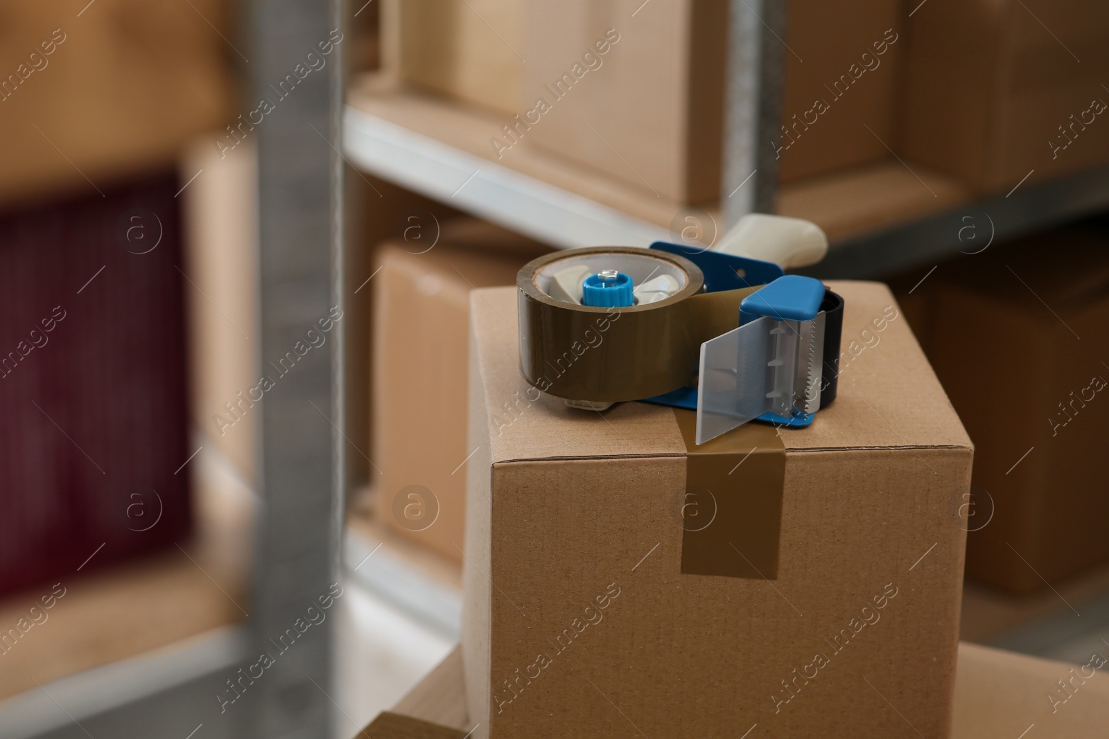 Photo of Adhesive tape dispenser on cardboard box indoors. Space for text