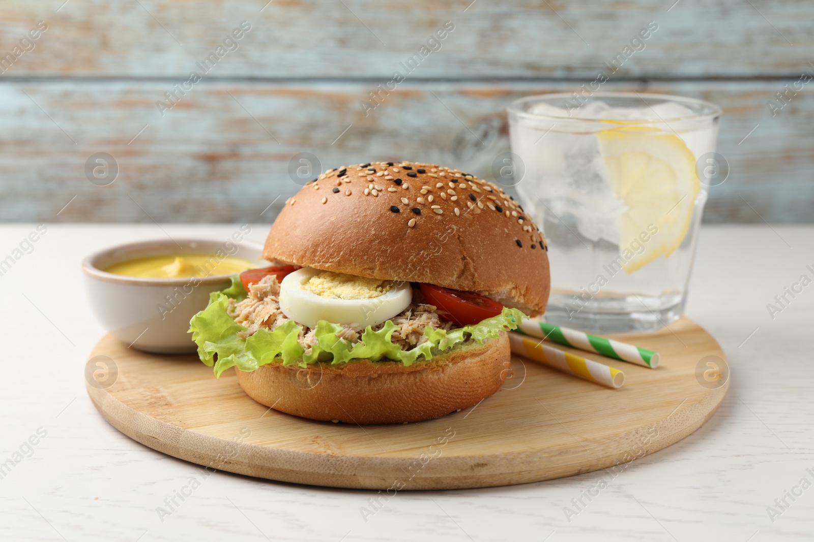 Photo of Delicious sandwich with tuna, boiled egg, vegetables served with mustard sauce and water with lemon on white table