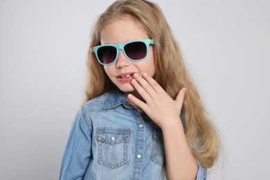 Girl in stylish sunglasses on light grey background