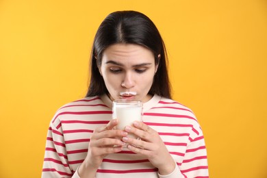 Cute woman with milk mustache drinking tasty dairy drink on yellow background