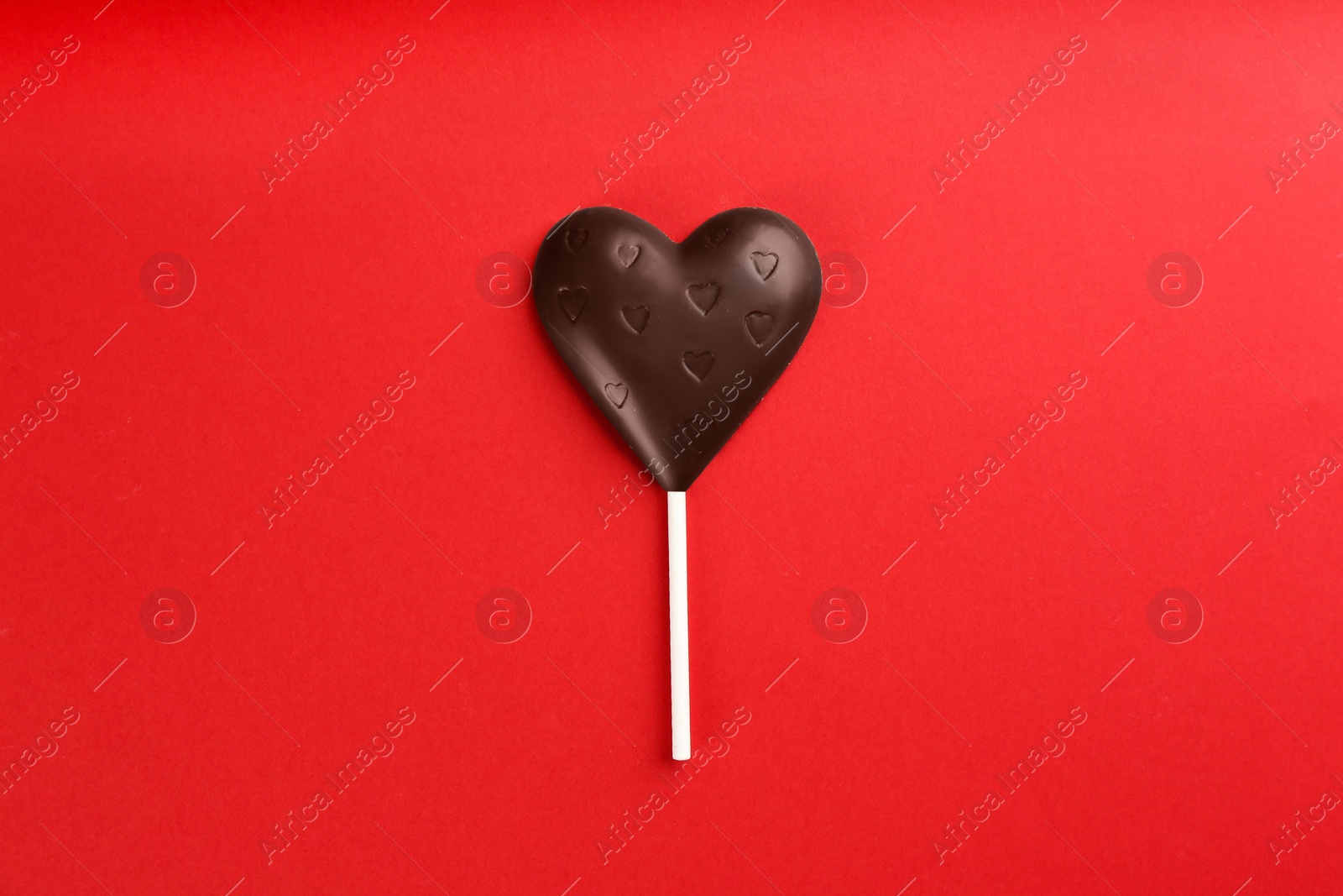 Photo of Chocolate heart shaped lollipop on red background, top view