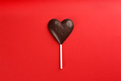 Chocolate heart shaped lollipop on red background, top view