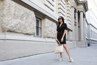 Photo of Young woman with stylish bag on city street. Space for text