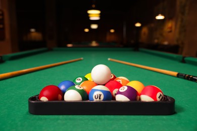 Photo of Plastic triangle rack with billiard balls and cues on green table indoors, space for text