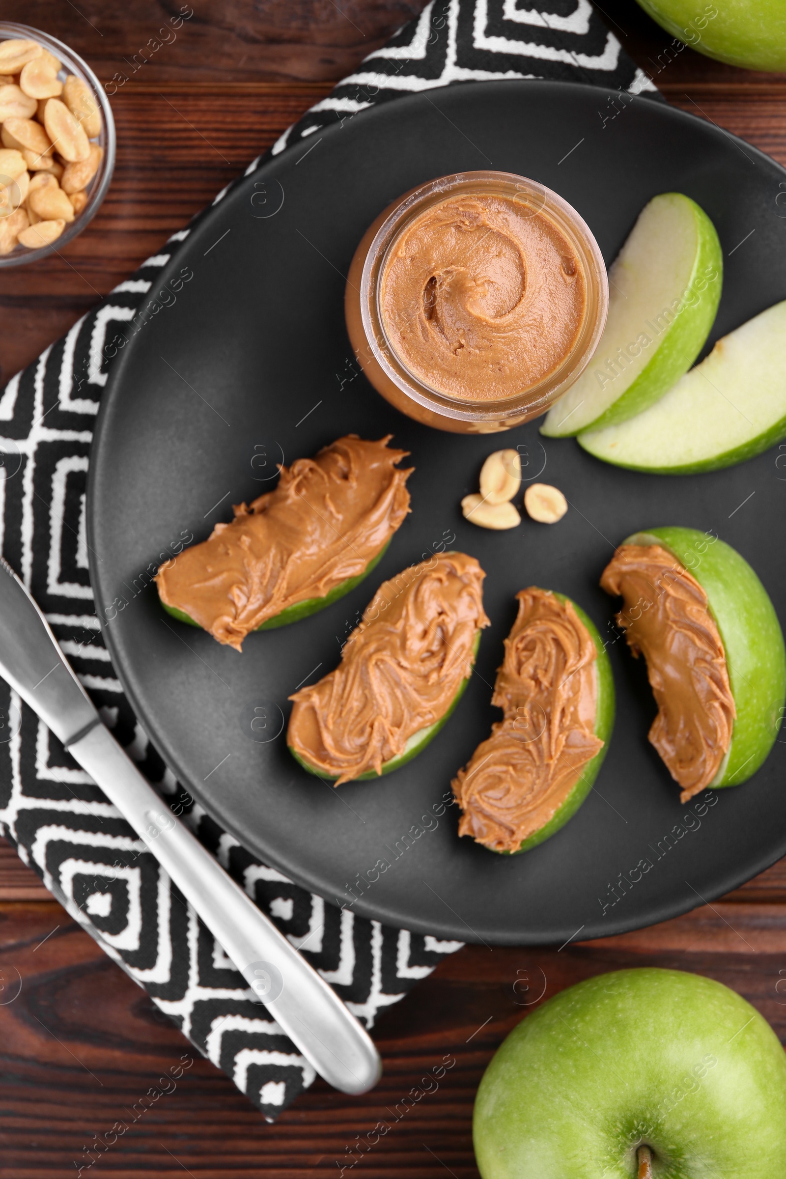 Photo of Slices of fresh green apple with peanut butter on wooden table, flat lay