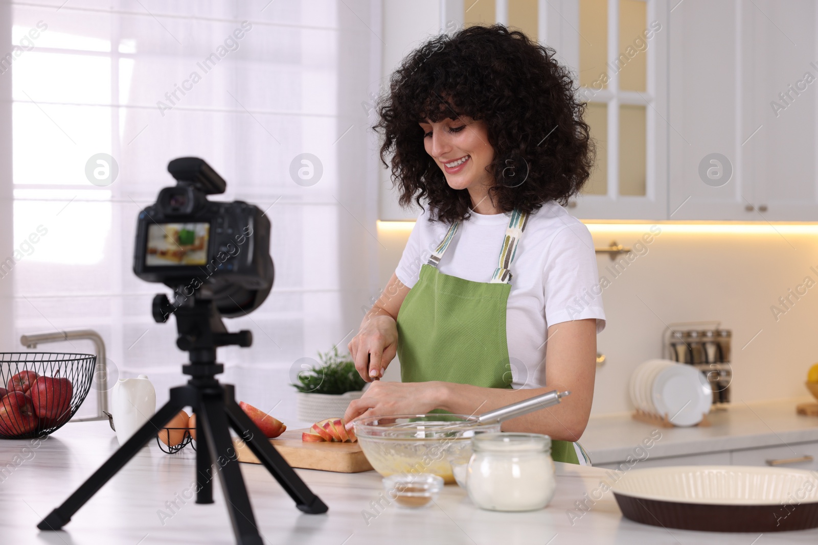 Photo of Smiling food blogger cooking while recording video in kitchen