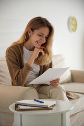 Happy woman reading letter on sofa at home
