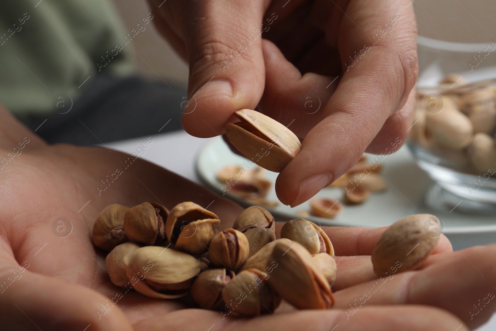 Photo of Woman holding tasty roasted pistachio nuts at table, closeup