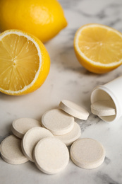 Bottle with vitamin pills and lemons on white marble table, closeup