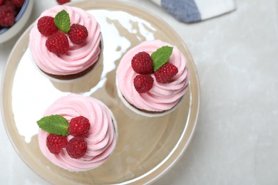 Photo of Delicious cupcakes with cream and raspberries on light grey marble table, flat lay
