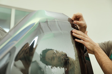 Worker tinting car window with foil in workshop, closeup