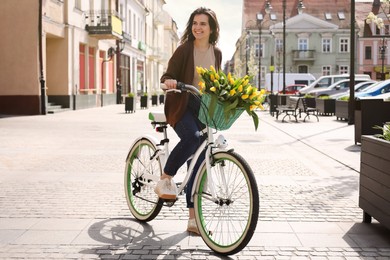 Beautiful woman with bicycle and bouquet of yellow tulips on city street