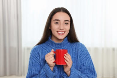 Photo of Happy young woman holding red ceramic mug at home