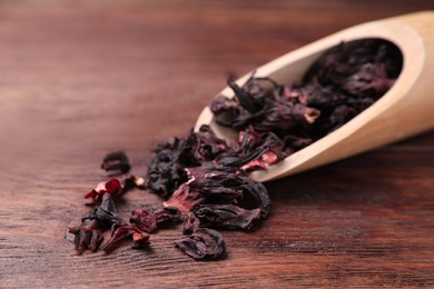 Photo of Scoop with dry hibiscus tea on wooden table, closeup