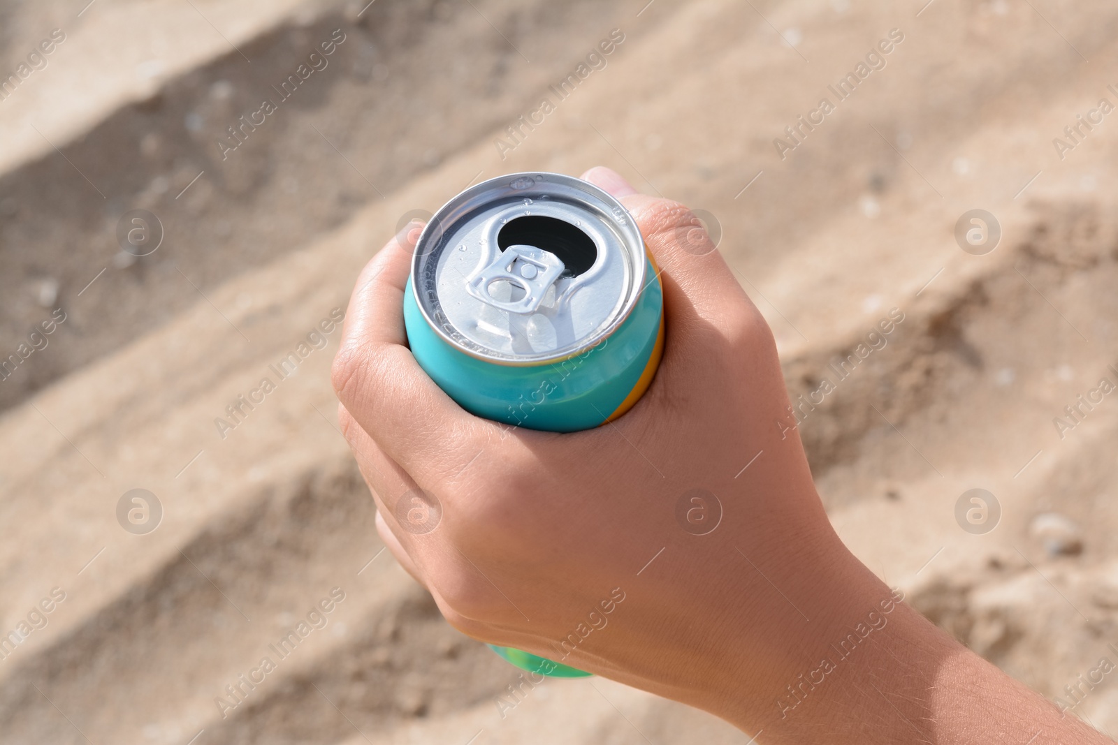 Photo of Woman holding aluminum can with beverage on sand, closeup