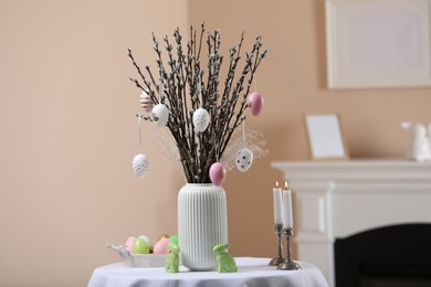 Photo of Pussy willow branches with festively decorated eggs, Easter bunnies and candles on table indoors