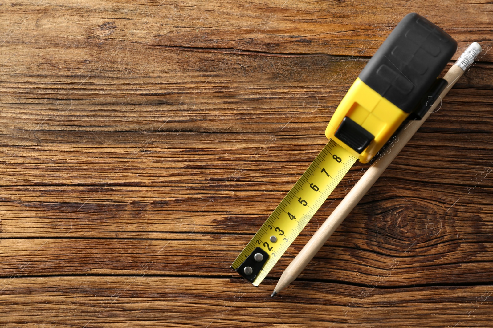 Photo of Metal measuring tape and pencil on wooden background, top view. Space for text