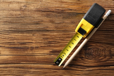 Metal measuring tape and pencil on wooden background, top view. Space for text