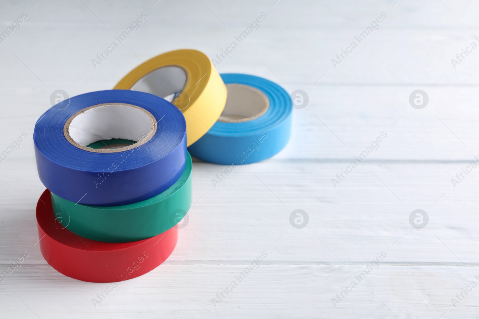 Photo of Colorful insulating tapes on white wooden table, space for text