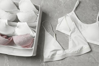 Organizer with women's underwear and beautiful bras on light grey marble table, flat lay